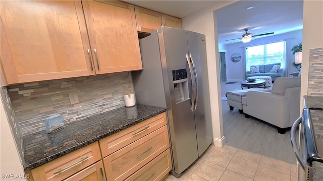 kitchen with stainless steel fridge, light tile patterned floors, decorative backsplash, ceiling fan, and dark stone counters