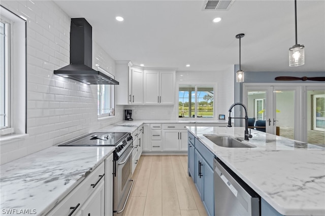 kitchen featuring appliances with stainless steel finishes, pendant lighting, wall chimney exhaust hood, white cabinets, and sink