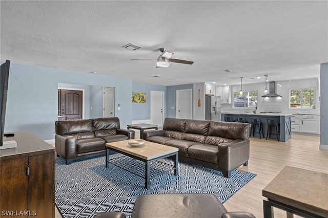 living room featuring ceiling fan, sink, a textured ceiling, and light wood-type flooring