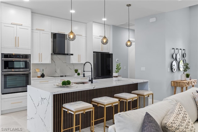 kitchen featuring an island with sink, wall chimney exhaust hood, a breakfast bar area, and black appliances