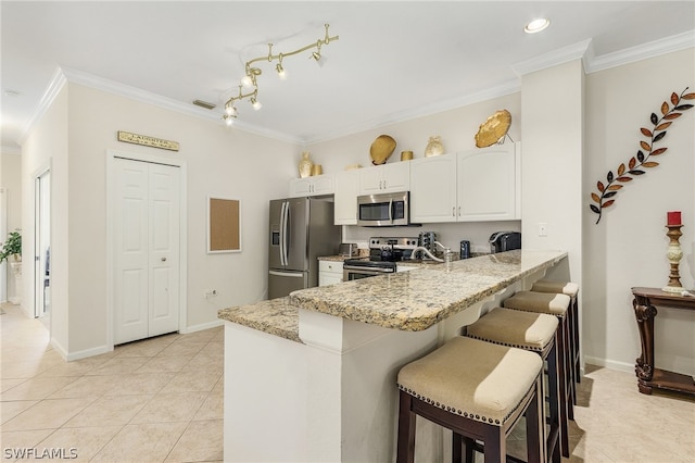 kitchen featuring a breakfast bar, stainless steel appliances, light tile floors, white cabinets, and rail lighting