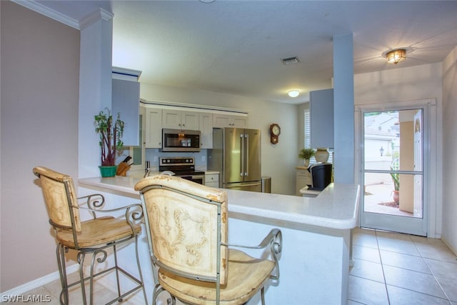 kitchen with white cabinetry, a breakfast bar area, light tile patterned floors, kitchen peninsula, and stainless steel appliances