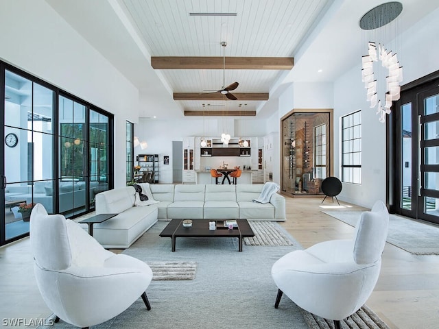 living room with a high ceiling, beam ceiling, ceiling fan, and light wood-type flooring