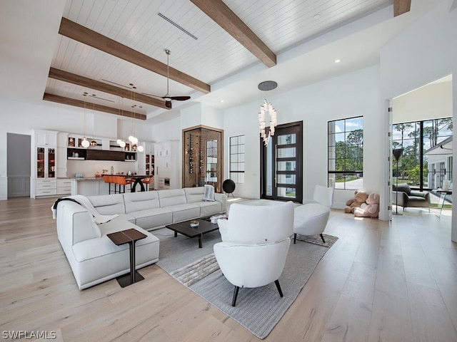 living room featuring beam ceiling, ceiling fan with notable chandelier, a towering ceiling, and light wood-type flooring