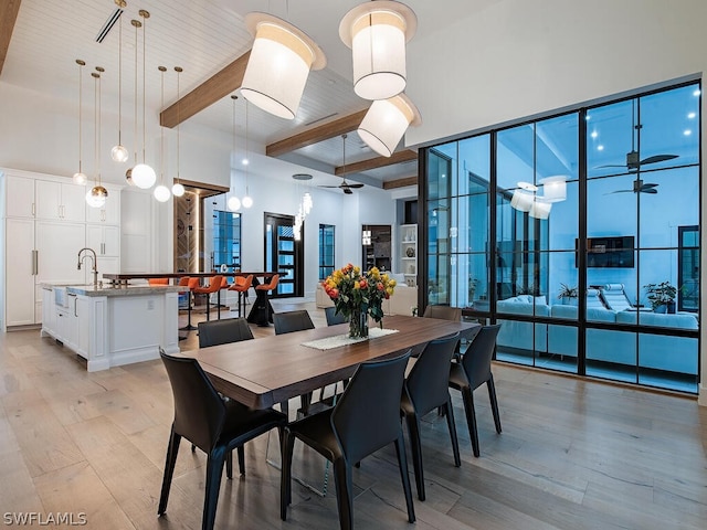 dining area featuring sink, light hardwood / wood-style floors, ceiling fan, and a towering ceiling