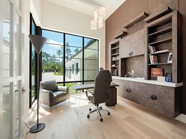 office with built in shelves, a high ceiling, and light hardwood / wood-style flooring