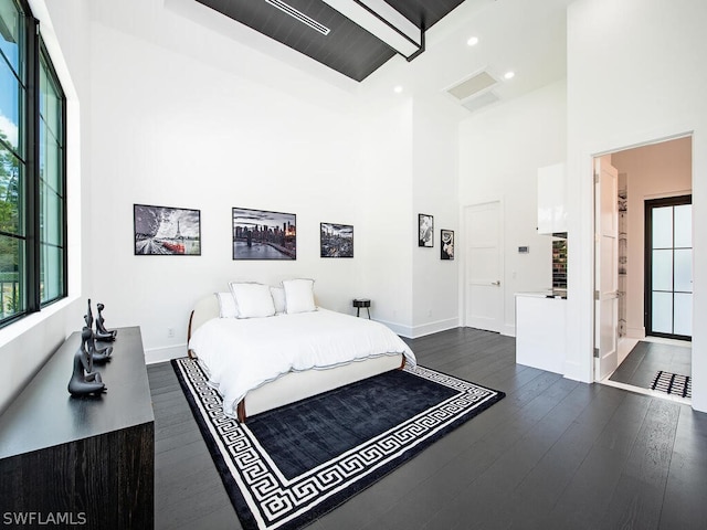 bedroom featuring beam ceiling, dark hardwood / wood-style flooring, ensuite bathroom, and a high ceiling