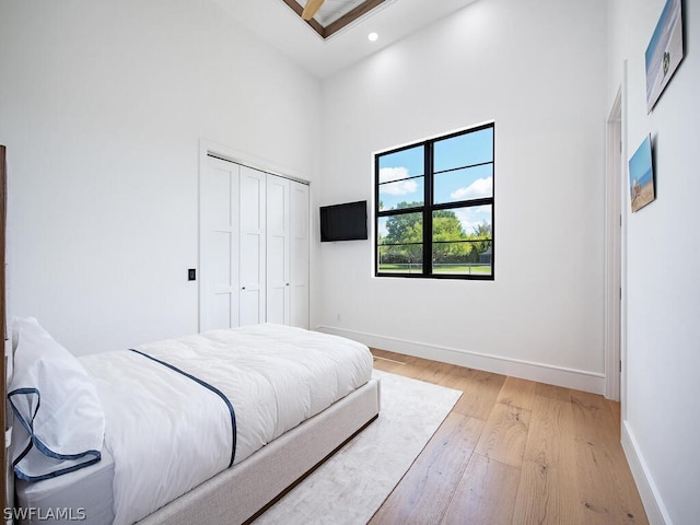 bedroom with light hardwood / wood-style floors, a closet, and a towering ceiling