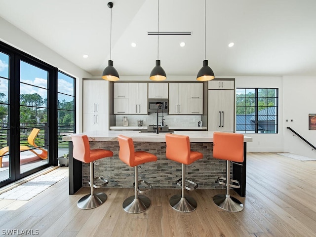 kitchen with backsplash, hanging light fixtures, a breakfast bar, and light hardwood / wood-style flooring