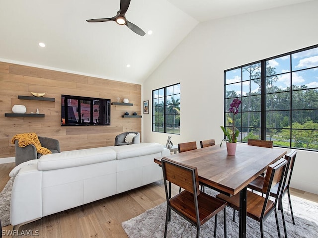 dining area with wood walls, high vaulted ceiling, ceiling fan, and light wood-type flooring