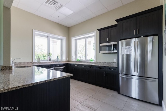 kitchen with appliances with stainless steel finishes, light stone counters, a drop ceiling, sink, and light tile patterned floors