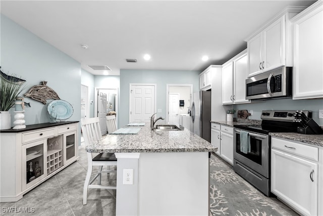 kitchen featuring stainless steel appliances, a kitchen island with sink, sink, dark stone countertops, and white cabinets