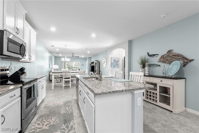 kitchen featuring dark stone counters, stainless steel appliances, sink, a center island with sink, and white cabinetry