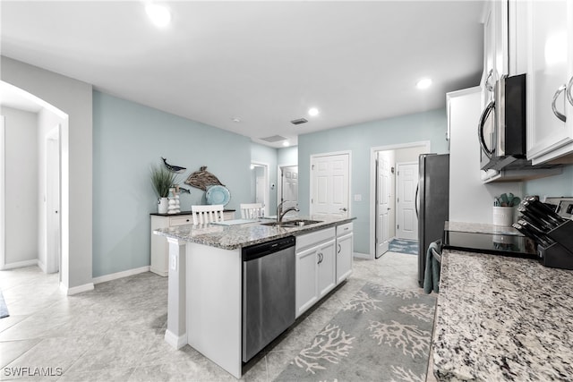 kitchen featuring white cabinetry, sink, stainless steel appliances, light stone counters, and an island with sink