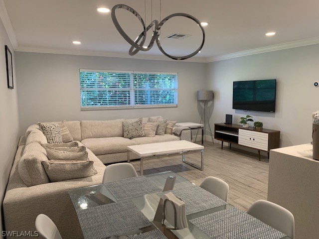 living room with a notable chandelier, light wood-type flooring, and crown molding