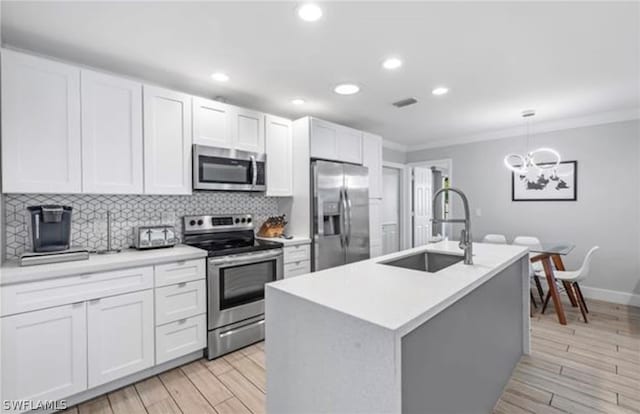 kitchen with an island with sink, sink, hanging light fixtures, appliances with stainless steel finishes, and an inviting chandelier