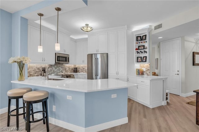 kitchen featuring decorative light fixtures, white cabinetry, sink, kitchen peninsula, and stainless steel appliances