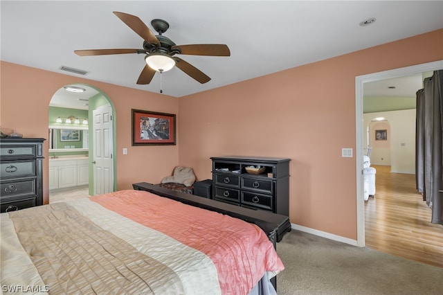 bedroom with ceiling fan, light colored carpet, and ensuite bathroom