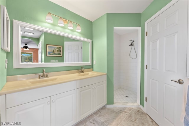 bathroom with dual bowl vanity, tile flooring, tiled shower, and ceiling fan