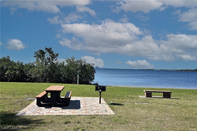 surrounding community featuring a water view, a lawn, and a patio