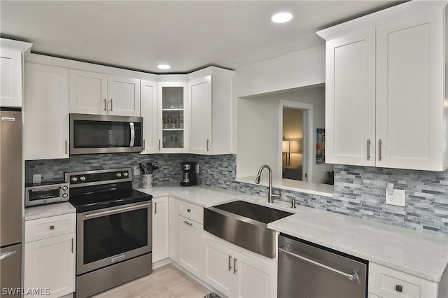 kitchen featuring light stone countertops, white cabinetry, backsplash, appliances with stainless steel finishes, and sink