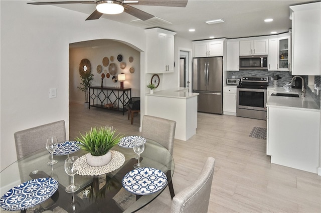 kitchen featuring ceiling fan, sink, backsplash, stainless steel appliances, and white cabinetry