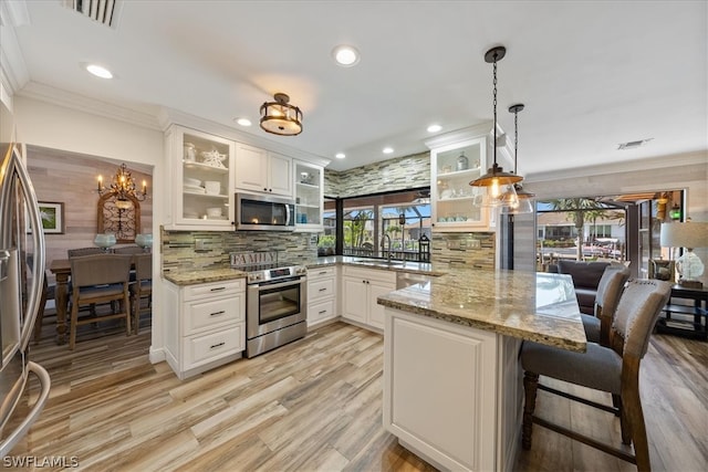 kitchen with light stone counters, backsplash, stainless steel appliances, an inviting chandelier, and decorative light fixtures