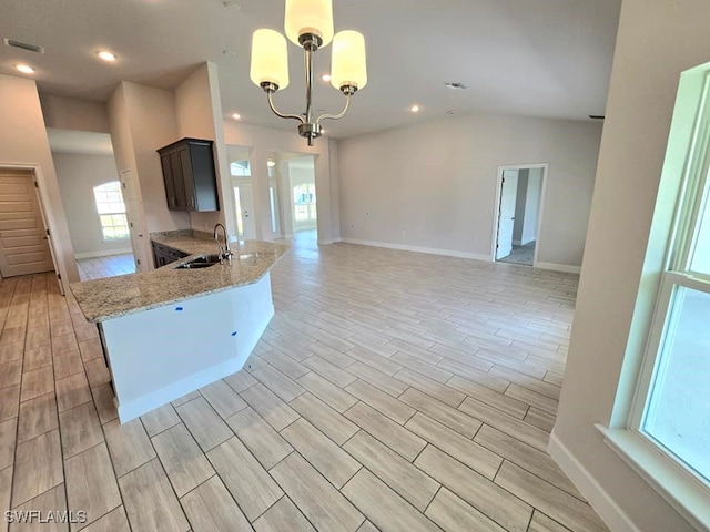 kitchen with sink, light hardwood / wood-style flooring, light stone counters, and kitchen peninsula