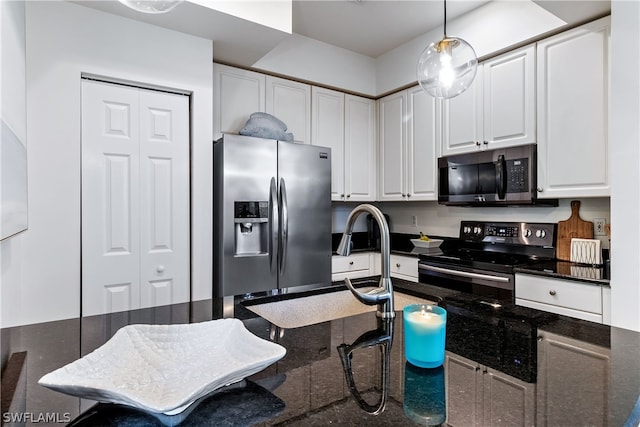 kitchen featuring dark stone countertops, white cabinets, appliances with stainless steel finishes, a breakfast bar area, and hanging light fixtures