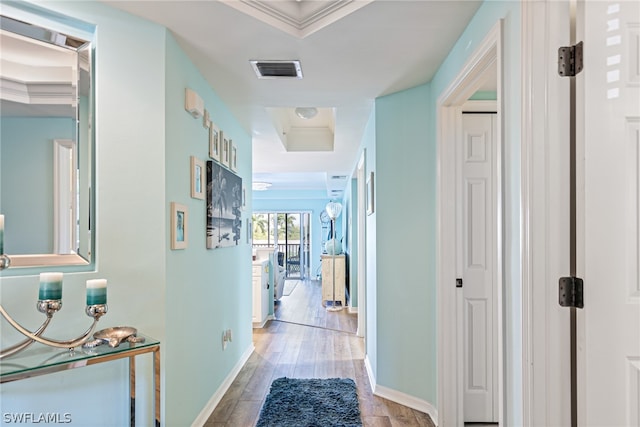 corridor with a raised ceiling, crown molding, and light wood-type flooring