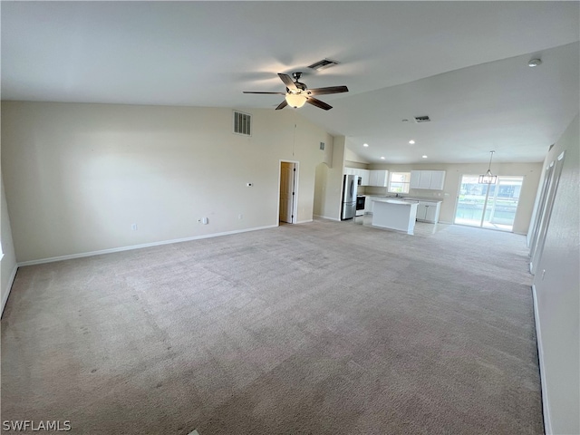 unfurnished living room with high vaulted ceiling, light colored carpet, and ceiling fan with notable chandelier