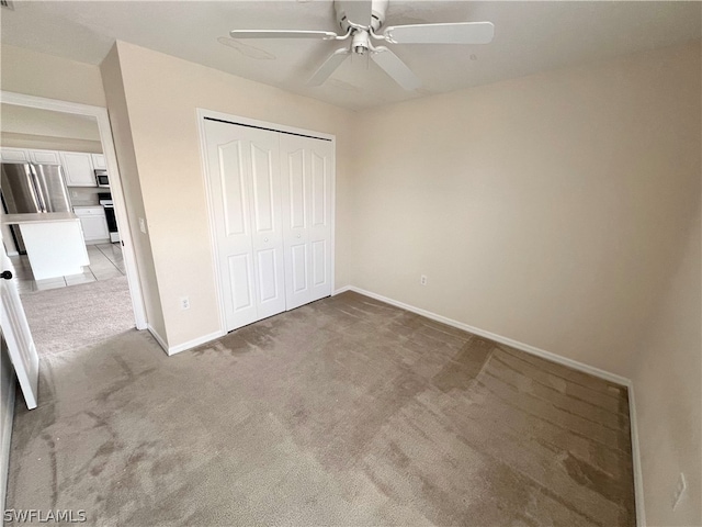 unfurnished bedroom featuring a closet, light carpet, stainless steel fridge, and ceiling fan