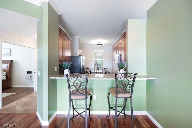 kitchen featuring dark hardwood / wood-style flooring, light stone counters, kitchen peninsula, stainless steel appliances, and crown molding