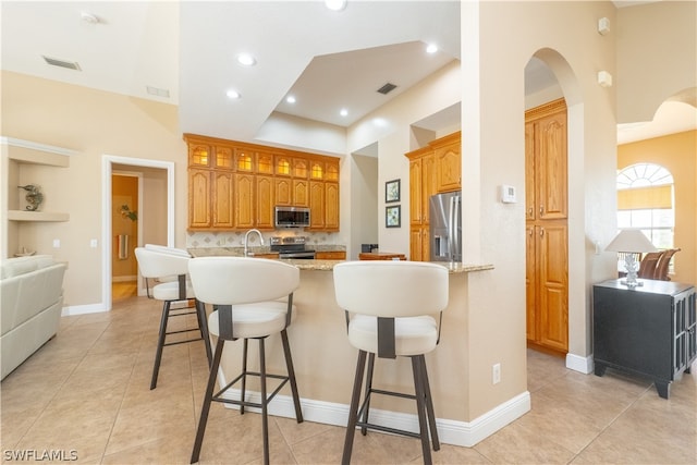 kitchen featuring a kitchen breakfast bar, light tile floors, tasteful backsplash, appliances with stainless steel finishes, and light stone counters