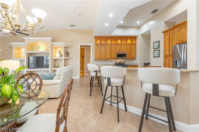 kitchen featuring light tile floors, light stone counters, appliances with stainless steel finishes, a kitchen bar, and a notable chandelier