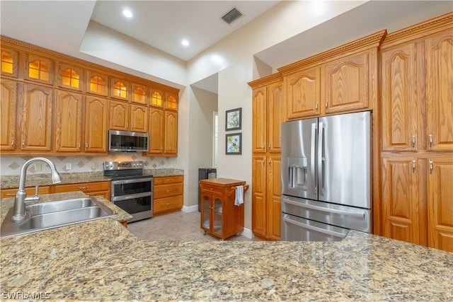 kitchen with stainless steel appliances, light tile floors, light stone countertops, tasteful backsplash, and sink