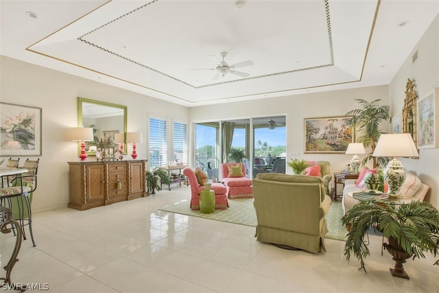 tiled living room with ceiling fan and a tray ceiling