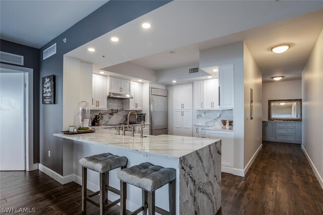 kitchen with built in fridge, tasteful backsplash, dark hardwood / wood-style flooring, white cabinets, and kitchen peninsula