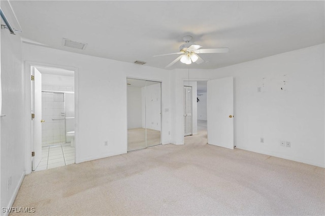 unfurnished bedroom with light colored carpet, ensuite bath, ceiling fan, and multiple closets