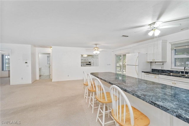 kitchen featuring a breakfast bar, light colored carpet, sink, white cabinets, and white fridge