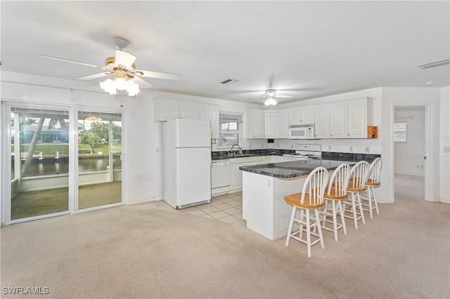 kitchen featuring white appliances, light colored carpet, sink, white cabinets, and a breakfast bar area