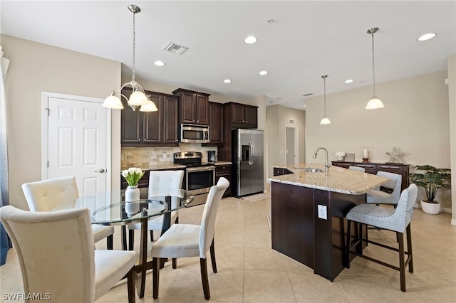 kitchen with hanging light fixtures, appliances with stainless steel finishes, a breakfast bar area, light stone countertops, and tasteful backsplash