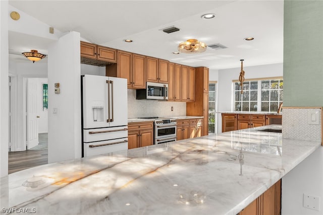 kitchen featuring kitchen peninsula, light stone counters, stainless steel appliances, tasteful backsplash, and light wood-type flooring