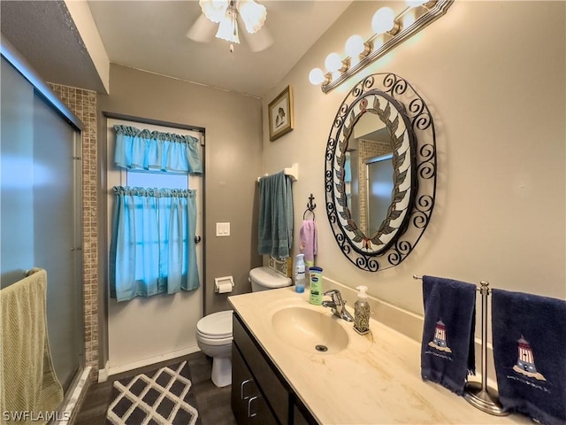 bathroom featuring ceiling fan, a shower with door, vanity, and toilet