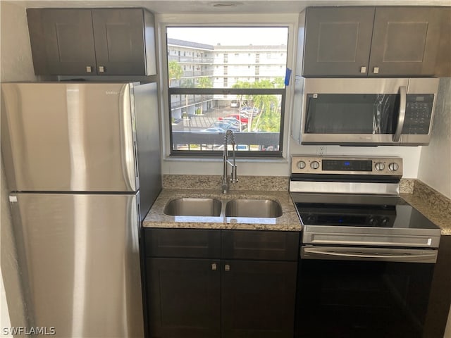 kitchen with light stone countertops, stainless steel appliances, dark brown cabinets, and sink