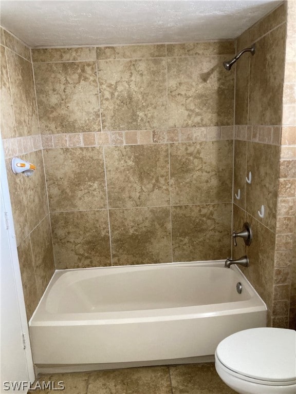 bathroom featuring tiled shower / bath combo, tile flooring, a textured ceiling, and toilet