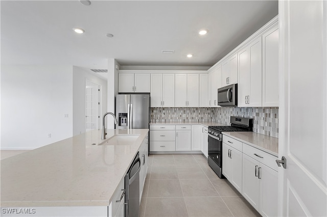 kitchen with white cabinets, sink, an island with sink, appliances with stainless steel finishes, and light stone counters