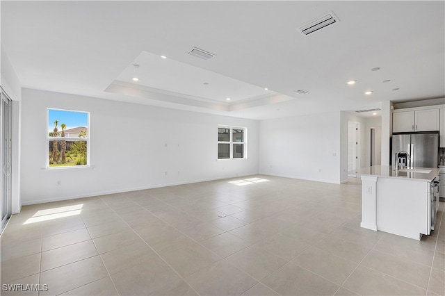 unfurnished living room featuring a raised ceiling and light tile patterned floors