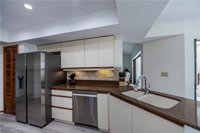 kitchen featuring white cabinets, dark stone countertops, backsplash, light hardwood / wood-style floors, and stainless steel appliances