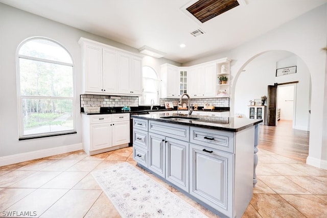 kitchen with white cabinetry, a kitchen island with sink, light tile flooring, and sink